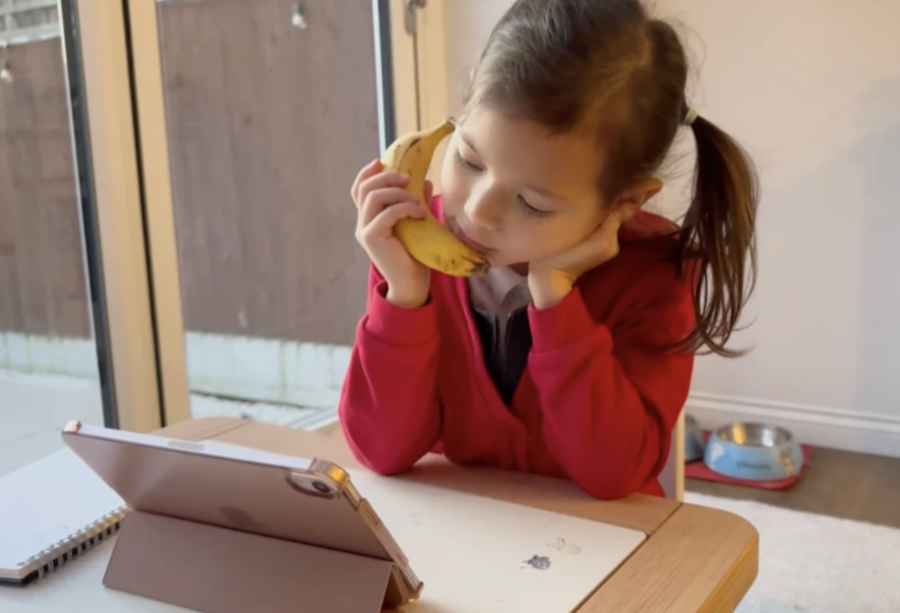 Niña merendando una banana mientras sigue su clase online de Diluu